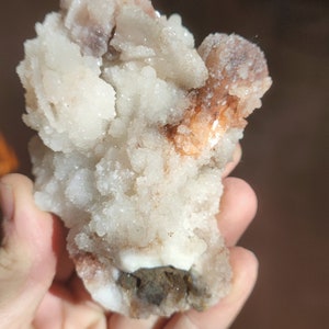 Könnte beinhalten: Ein Cluster aus weißen und orangefarbenen Kristallen mit einer rauen, strukturierten Oberfläche. Die Kristalle sind in einem zufälligen, organischen Muster angeordnet.