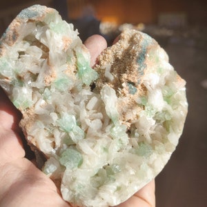 Könnte beinhalten: Ein herzförmiger Geode mit weißen und grünen Kristallen. Der Geode ist aufgebrochen und zeigt die Kristalle im Inneren.