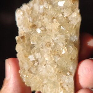 Pu&ograve; includere: Un ammasso di piccoli cristalli trasparenti e traslucidi con una tonalit&agrave; marrone chiaro. I cristalli sono raggruppati in una forma irregolare e ruvida.