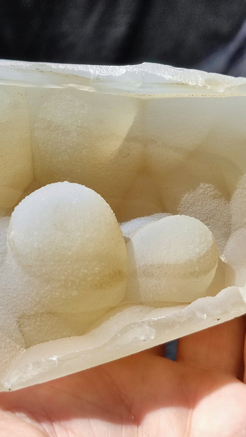 May include: A close-up of a white, translucent, geode with a rough, textured surface. The geode is filled with small, white, crystal formations.