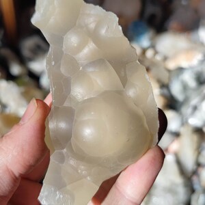 K&ouml;nnte beinhalten: Ein durchscheinender wei&szlig;er Achat mit einer blasigen, strukturierten Oberfl&auml;che. Der Achat hat eine milchig wei&szlig;e Farbe und ist unregelm&auml;&szlig;ig geformt.