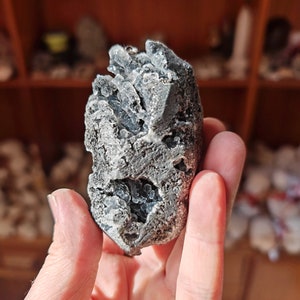 May include: A gray and white crystal cluster with a rough, textured surface. The crystal has a unique, organic shape and is reminiscent of a small mountain.