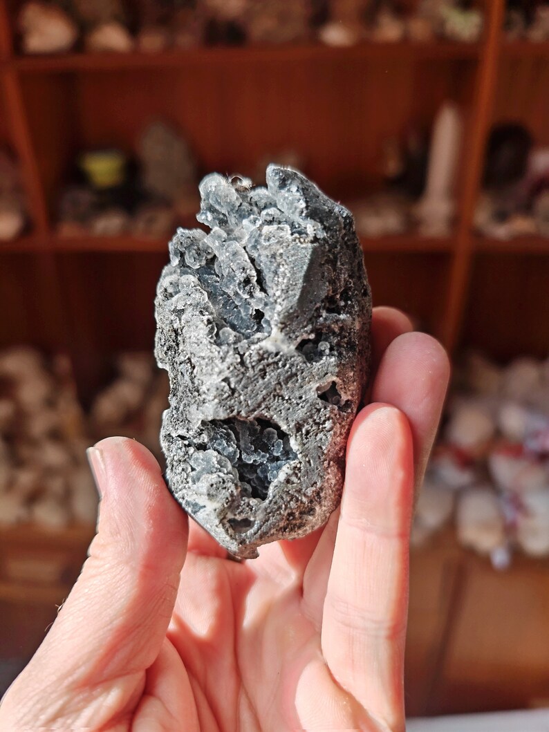 May include: A gray and white crystal cluster with a rough, textured surface. The crystal has a unique, organic shape and is reminiscent of a small mountain.