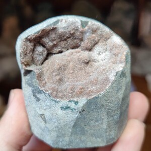 Könnte beinhalten: Ein grauer Geode mit einem gebrochenen, offenen Abschnitt, der eine braune und weiße Kristallformation freilegt.