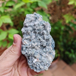 May include: A cluster of blue celestite crystals with a white, sparkly, and translucent appearance. The crystals are clustered together in a rough, natural formation.