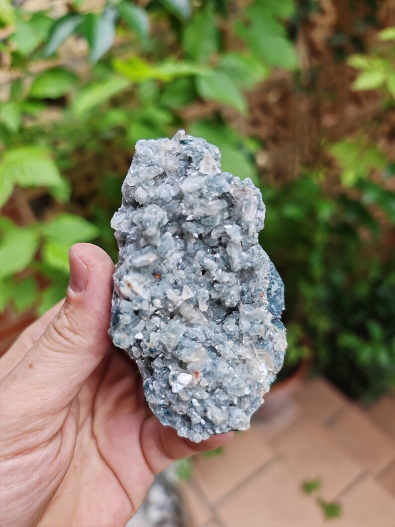 May include: A cluster of blue celestite crystals with a white, sparkly, and translucent appearance. The crystals are clustered together in a rough, natural formation.