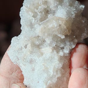 Puede incluir: Un cúmulo de cristales blancos translúcidos con una superficie rugosa y texturizada. Los cristales están dispuestos en un patrón aleatorio, creando una exhibición única e interesante.