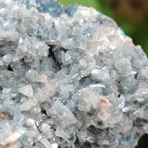 May include: A cluster of clear, glassy crystals embedded in a dark green, rocky matrix. The crystals have a sharp, angular shape and are arranged in a random pattern.