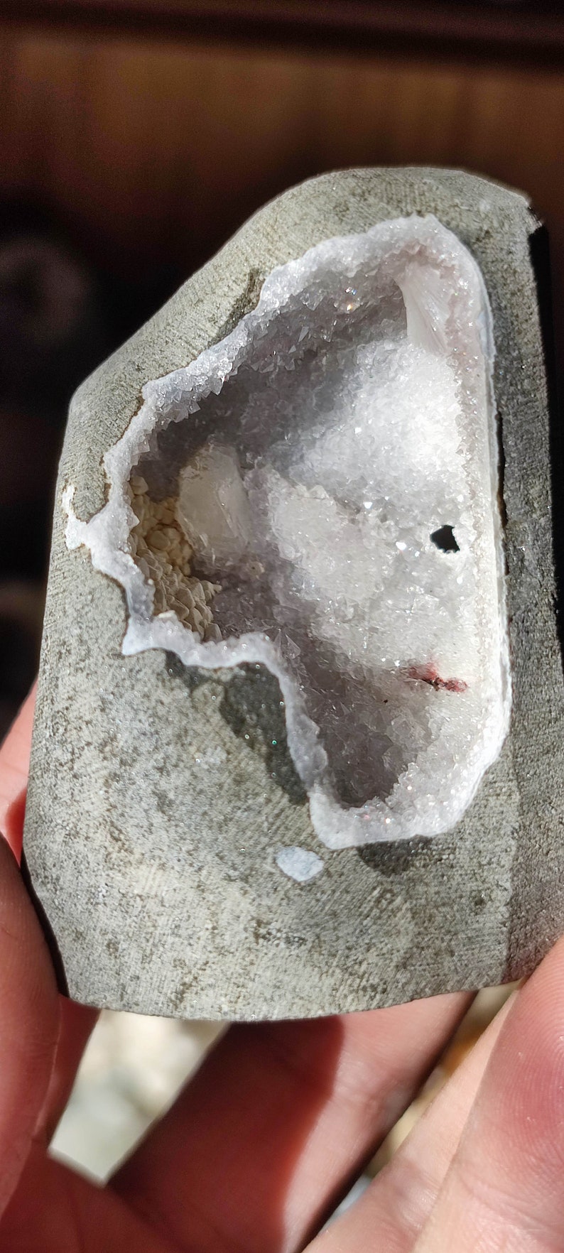 K&ouml;nnte beinhalten: Ein grauer Stein mit einer ausgeh&ouml;hlten Mitte, die mit wei&szlig;en Kristallen gef&uuml;llt ist. Die Kristalle haben einen leichten violetten Farbton und funkeln im Licht.