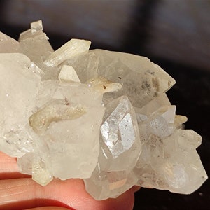 May include: A cluster of clear quartz crystals with a rough, natural texture. The crystals are clustered together in a random formation, creating a unique and interesting display.