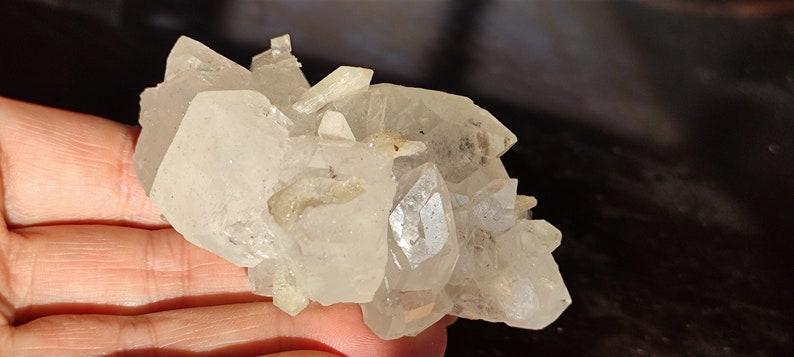 May include: A cluster of clear quartz crystals with a rough, natural texture. The crystals are clustered together in a random formation, creating a unique and interesting display.