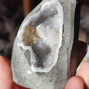 K&ouml;nnte beinhalten: Ein grauer Stein mit einer hohlen Mitte, die mit wei&szlig;en Kristallen gef&uuml;llt ist. Die Kristalle sind zusammengedr&auml;ngt und haben ein glitzerndes Aussehen.
