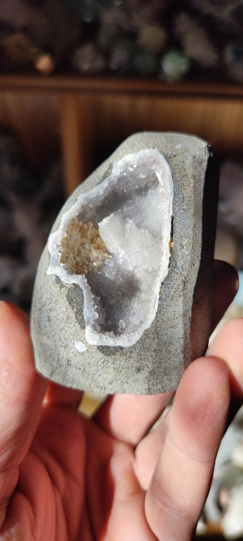 K&ouml;nnte beinhalten: Ein grauer Stein mit einer hohlen Mitte, die mit wei&szlig;en Kristallen gef&uuml;llt ist. Die Kristalle sind zusammengedr&auml;ngt und haben ein glitzerndes Aussehen.