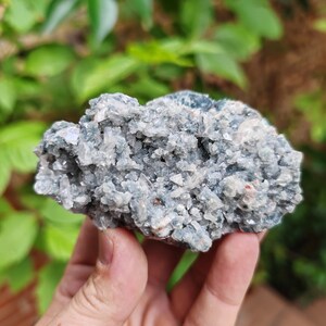 May include: A cluster of grey and white crystals with a green hue. The crystals are arranged in a rough, natural shape.