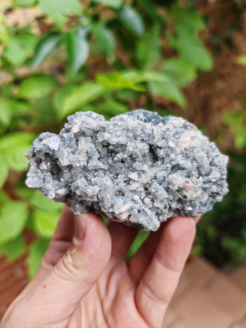 May include: A cluster of grey and white crystals with a green hue. The crystals are arranged in a rough, natural shape.