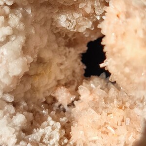 Könnte beinhalten: Eine Geode mit einem hohlen Zentrum, gefüllt mit weißen und rosa Kristallen. Die Kristalle sind zusammengedrängt und haben eine raue, strukturierte Oberfläche.