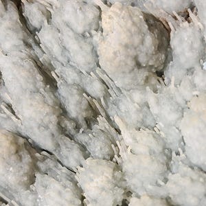 Puede incluir: Primer plano de una formaci&oacute;n mineral azul claro con una superficie texturizada. El mineral tiene una estructura cristalina con peque&ntilde;os grupos redondeados y finas protuberancias en forma de aguja, creando una apariencia org&aacute;nica &uacute;nica.