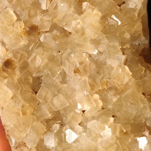 Pu&ograve; includere: Un ammasso di cristalli traslucidi di colore marrone chiaro con una texture ruvida e naturale. I cristalli sono disposti in uno schema denso e irregolare, creando un pezzo visivamente interessante e unico.