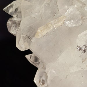 May include: A cluster of clear quartz crystals with a pointed shape. The crystals are arranged in a cluster, with some of the crystals pointing upwards and others pointing downwards. The crystals are translucent and have a slight sparkle.