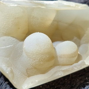 May include: A white geode with a smooth, shiny exterior and a hollow interior filled with white, round, crystal formations.