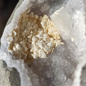 K&ouml;nnte beinhalten: Nahaufnahme einer Geode mit einer wei&szlig;en Kristallverkleidung und einem Cluster kleiner, wei&szlig;er Kristalle im Inneren. Die Geode ist teilweise ge&ouml;ffnet und gibt den Blick auf die Kristalle im Inneren frei.