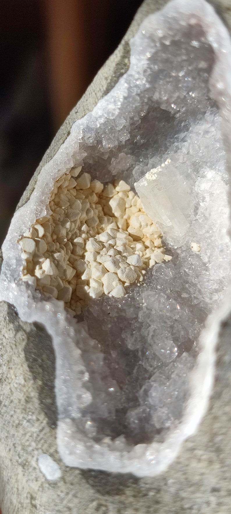 K&ouml;nnte beinhalten: Nahaufnahme einer Geode mit einer wei&szlig;en Kristallverkleidung und einem Cluster kleiner, wei&szlig;er Kristalle im Inneren. Die Geode ist teilweise ge&ouml;ffnet und gibt den Blick auf die Kristalle im Inneren frei.