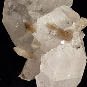 May include: A cluster of clear quartz crystals with a milky white hue. The crystals are arranged in a cluster, with some of the crystals pointing upwards and others pointing downwards. The crystals are translucent and have a slight sparkle.