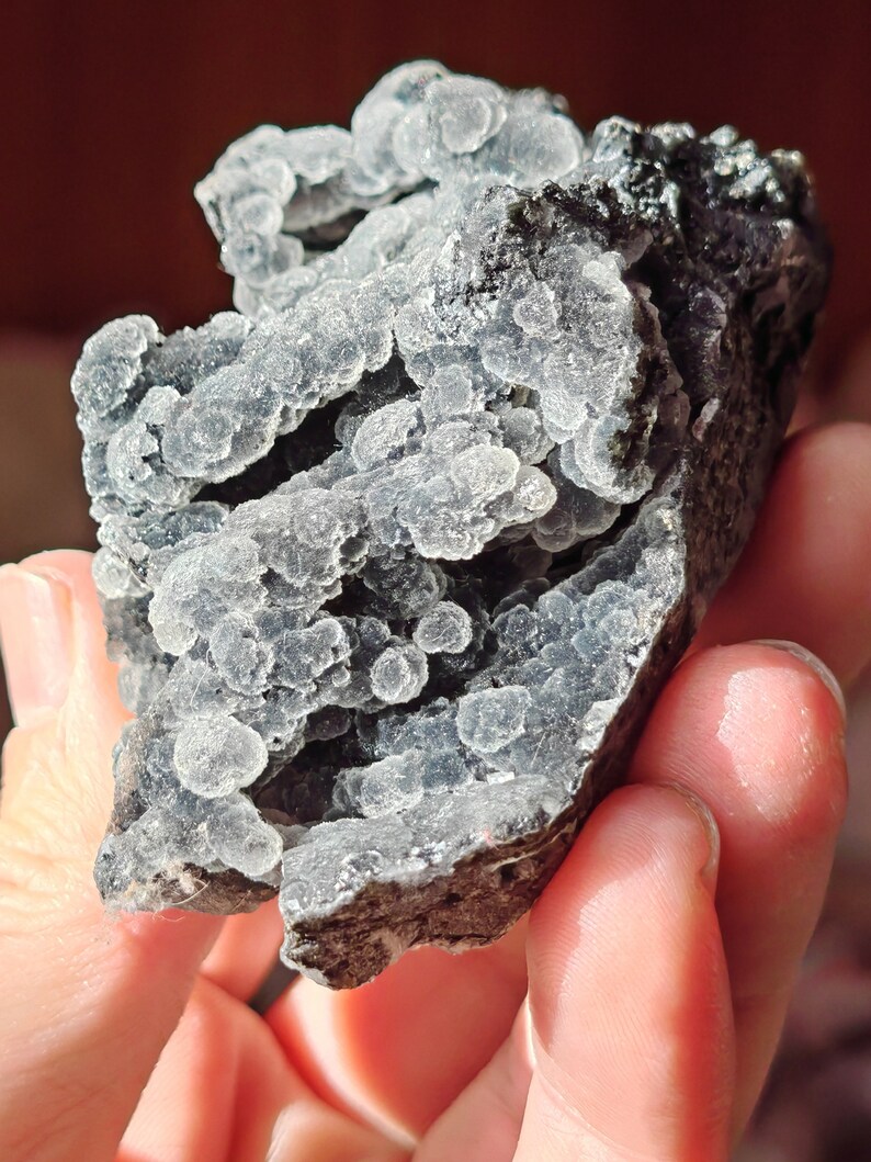 May include: A cluster of gray and black chalcedony with a bubbly texture. The chalcedony is translucent and has a light blue hue.