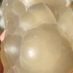 K&ouml;nnte beinhalten: Nahaufnahme eines hellbeigen, durchscheinenden, unregelm&auml;&szlig;ig geformten Steins mit einer glatten, abgerundeten Oberfl&auml;che. Der Stein hat eine einzigartige, blasenartige Textur.