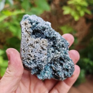 May include: A rough, green and grey rock with a crystalline texture. The rock has a natural, earthy look.