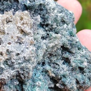 May include: A close-up of a rough, dark green and grey rock with a white, crystalline texture. The rock has a natural, earthy appearance.