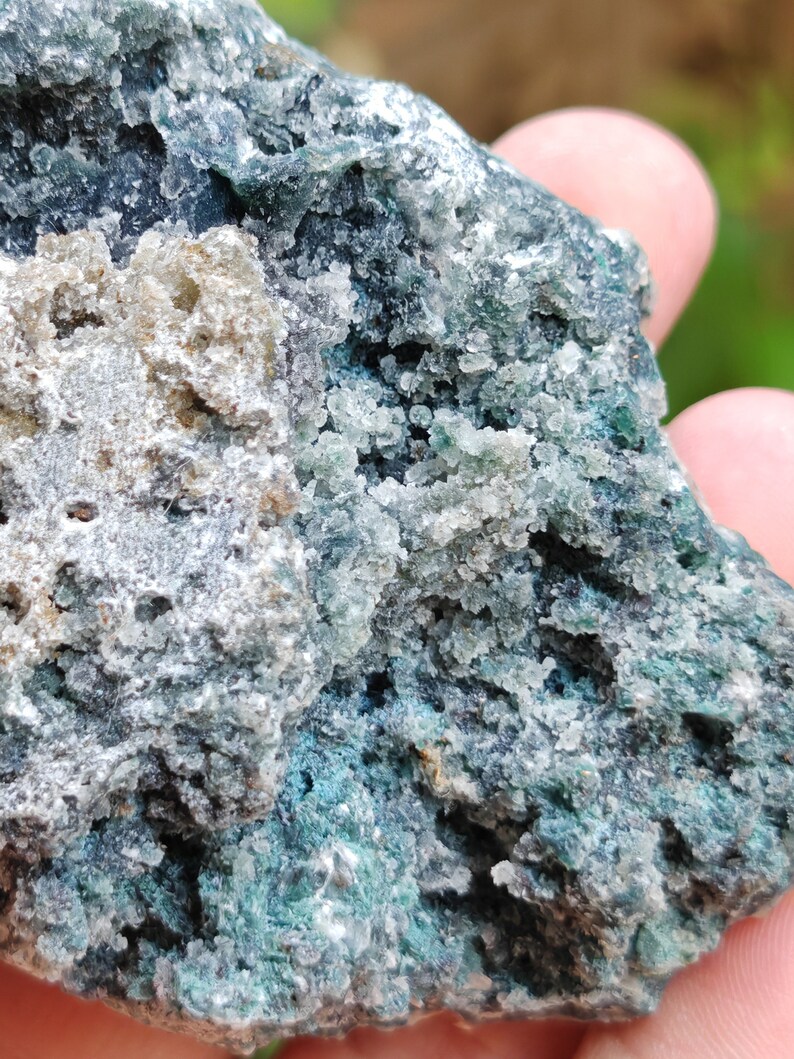 May include: A close-up of a rough, dark green and grey rock with a white, crystalline texture. The rock has a natural, earthy appearance.