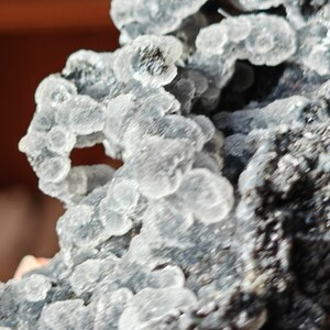 May include: A close-up of a gray and white mineral specimen with a rough, textured surface. The mineral has a cluster of small, white crystals.