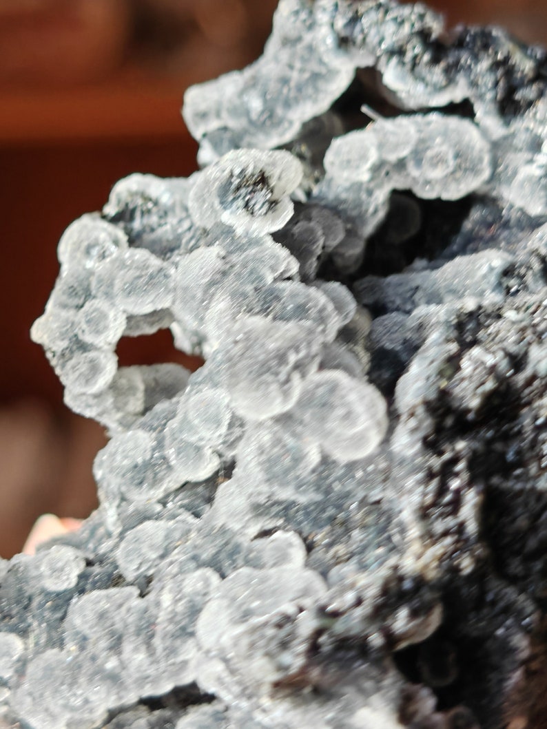May include: A close-up of a gray and white mineral specimen with a rough, textured surface. The mineral has a cluster of small, white crystals.