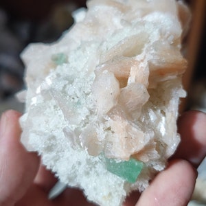 Könnte beinhalten: Ein Cluster aus rosa und weißen Celestit-Kristallen mit grünen Fluorit-Einschlüssen. Die Kristalle sind in einem natürlichen, organischen Muster angeordnet.