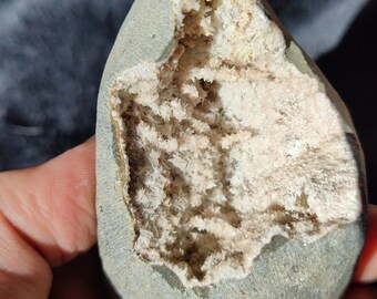 May include: A gray rock with a cavity filled with white crystals. The crystals are clustered together and have a rough, textured surface.
