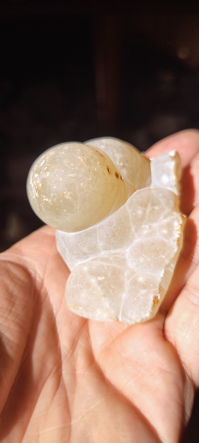 Może przedstawiać: Biała geoda agatowa z przezroczystym, mlecznobiałym wnętrzem i brązowymi oznaczeniami. Geoda ma kształt serca i gładką, polerowaną powierzchnię.