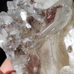 Könnte beinhalten: Ein Cluster aus klaren Quarzkristallen mit rotbraunen Einschlüssen. Die Kristalle sind in einer natürlichen Formation zusammengefügt und bilden eine einzigartige und interessante Darstellung.