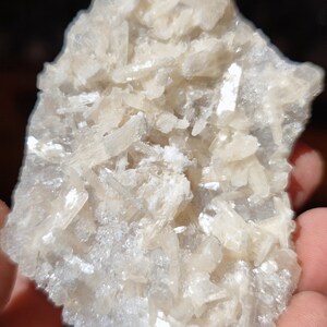 Könnte beinhalten: Ein Cluster aus weißen, durchscheinenden Kristallen mit einer rauen, strukturierten Oberfläche. Die Kristalle sind in einem zufälligen, organischen Muster angeordnet.