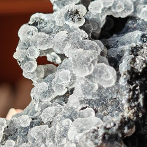 May include: Close-up of a gray and white mineral specimen with a rough, textured surface. The mineral has a cluster of small, white, round formations.