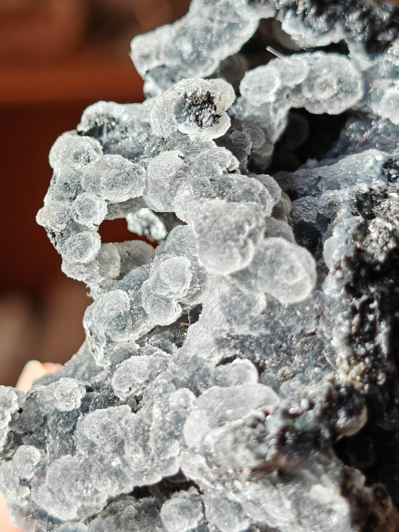 May include: Close-up of a gray and white mineral specimen with a rough, textured surface. The mineral has a cluster of small, white, round formations.