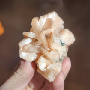 Könnte beinhalten: Ein Cluster aus hellorangen Selenitkristallen mit einigen grünen Einschlüssen. Die Kristalle sind durchscheinend und haben eine glatte, glasartige Oberfläche.