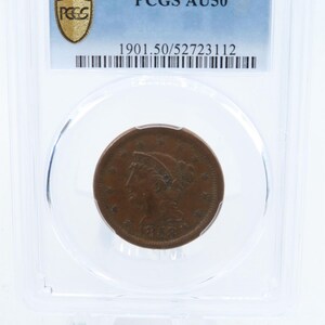 May include: A brown 1853 one-cent coin, encapsulated in a clear plastic holder. The coin features a profile of a woman and the text "1853". The holder has a label with "PCGS AU50" and other text.