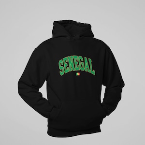 May include: Black hooded sweatshirt with the word "SENEGAL" in green, arched across the chest. The text has a white outline. Below the text is a small flag of Senegal. The sweatshirt has a front pocket and a hood.
