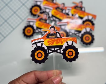 Könnte beinhalten: Ein Set mit sechs Monstertruck-Kuchen-Toppern, die ein Kindergesicht im Fahrersitz zeigen. Die Trucks sind orange und schwarz mit Flammen und dem Text "Monster Jam" an der Seite.