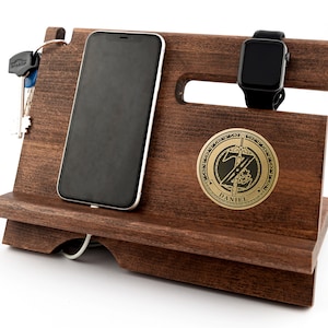 May include: A dark brown wooden phone and watch stand with a gold metal plaque that says "DANIEL". The stand has a slot for a phone, a watch holder, and a key hook.