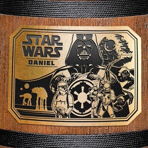 May include: A gold-colored metal plaque with a black and white image of Darth Vader and other Star Wars characters. The plaque has the text "STAR WARS DANIEL" on it.