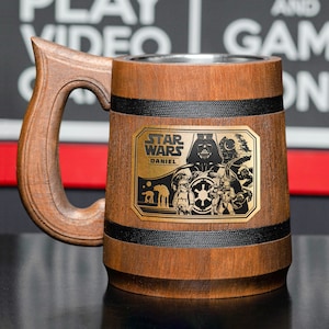 May include: A brown wooden beer stein with a black handle and a metal plaque featuring the Star Wars logo and the text "Star Wars" and "Daniel".