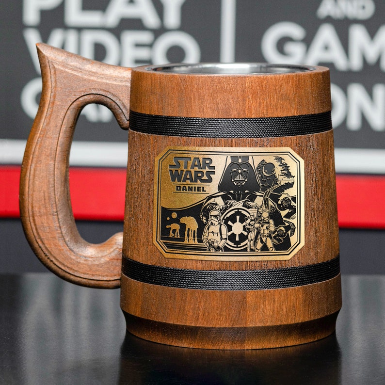 May include: A brown wooden beer stein with a black handle and a metal plaque featuring the Star Wars logo and the text "Star Wars" and "Daniel".