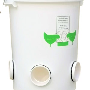 Puede incluir: Comedero automático para pollos de plástico blanco con un logotipo verde que dice "UpToDate Farmer" y dos pollos verdes a cada lado del logotipo. El comedero tiene tres aberturas en la parte inferior para que los pollos puedan acceder al alimento.